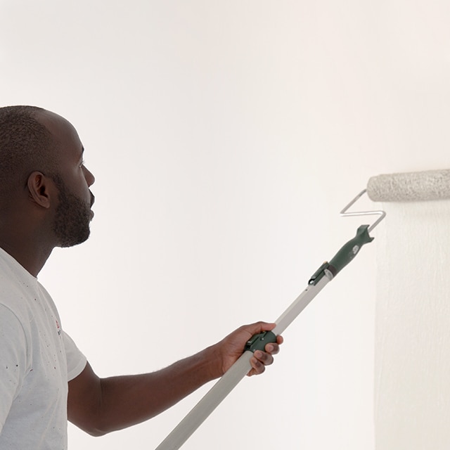Un peintre applique au rouleau de la peinture blanche sur un mur enduit d’apprêt. Un peintre applique au rouleau de la peinture blanche sur un mur enduit d’apprêt.