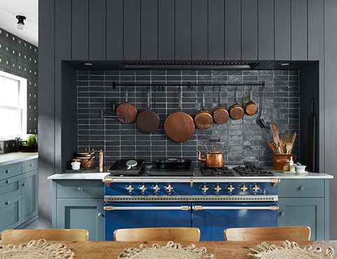 Cuisine accueillante avec armoires bleues, mur en planches à feuillure noires, dosseret noir, plafond blanc, cuisinière bleue, et table et chaises en bois. Cuisine accueillante avec armoires bleues, mur en planches à feuillure noires, dosseret noir, plafond blanc, cuisinière bleue, et table et chaises en bois.