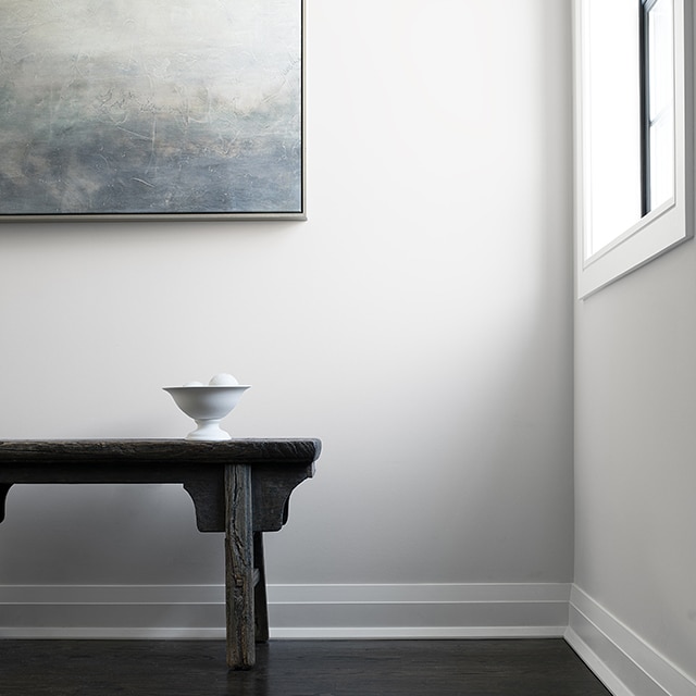 Un couloir présentant des murs et des moulures peints en blanc, un banc en bois noir et un tableau contemporain. Un couloir présentant des murs et des moulures peints en blanc, un banc en bois noir et un tableau contemporain.