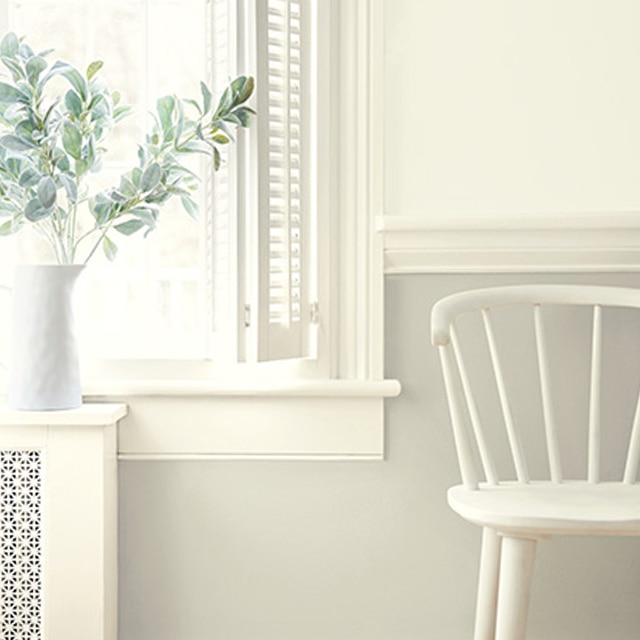Des nuances variées de peinture blanche sur les murs, les moulures et les lambris, et une chaise blanche près de la fenêtre. Des nuances variées de peinture blanche sur les murs, les moulures et les lambris, et une chaise blanche près de la fenêtre.