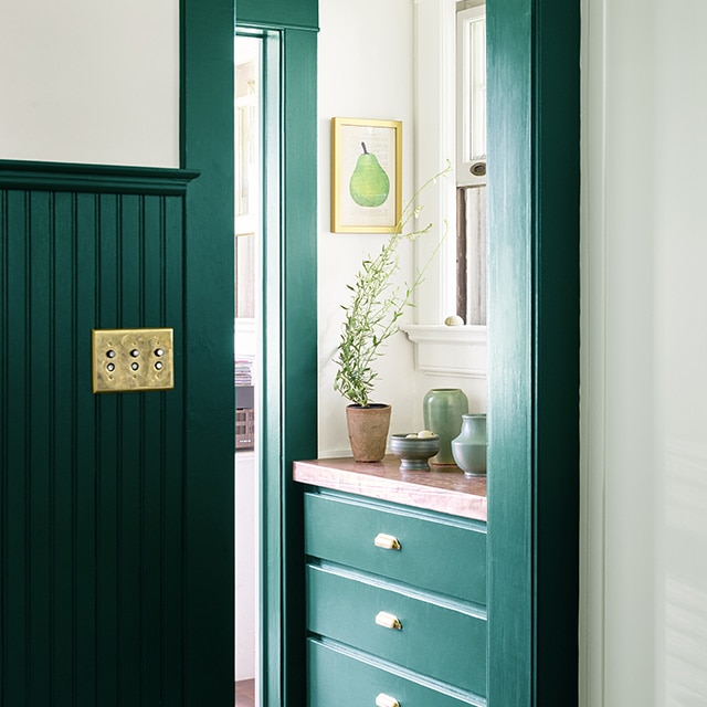 Hall d’entrée avec lambris d’appui, moulures et tiroirs encastrés d’une riche teinte de vert foncé en dessous d’une fenêtre et d’armoires murales vert pâle. Hall d’entrée avec lambris d’appui, moulures et tiroirs encastrés d’une riche teinte de vert foncé en dessous d’une fenêtre et d’armoires murales vert pâle.