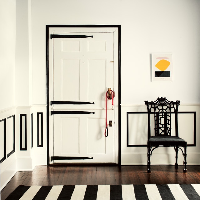 Cette pièce stylisée noir et blanc met en vedette des murs, plafond et porte de couleur blanche et des moulures et charnières décoratives de porte de couleur noire, une chaise noire et un tapis aux rayures noir et blanc. Cette pièce stylisée noir et blanc met en vedette des murs, plafond et porte de couleur blanche et des moulures et charnières décoratives de porte de couleur noire, une chaise noire et un tapis aux rayures noir et blanc.