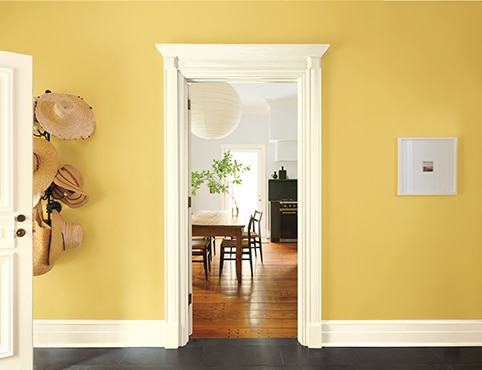 Joli vestibule jaune doré avec support mural à chapeaux, moulures blanches et porte blanche qui ouvre sur une cuisine gris pâle. Joli vestibule jaune doré avec support mural à chapeaux, moulures blanches et porte blanche qui ouvre sur une cuisine gris pâle.