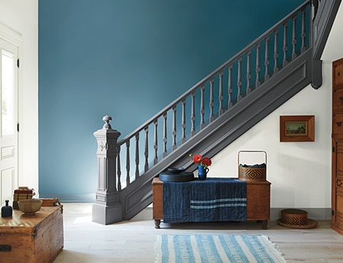 Spacieux vestibule avec escalier gris de style victorien, mur d’accent céruléen, murs et porte d’entrée gris pâle et coffres de rangement en bois d’époque. Spacieux vestibule avec escalier gris de style victorien, mur d’accent céruléen, murs et porte d’entrée gris pâle et coffres de rangement en bois d’époque.