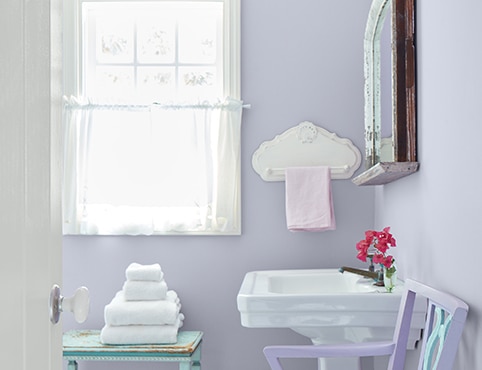 Salle de bains lumineuse aux murs violet pastel avec lavabo blanc, boiseries de fenêtre blanches et rideaux vaporeux blancs. Salle de bains lumineuse aux murs violet pastel avec lavabo blanc, boiseries de fenêtre blanches et rideaux vaporeux blancs.