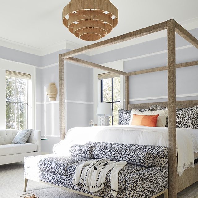 A bright and airy light-gray painted bedroom with white wall trim and ceiling, a modern four-poster bed, a fun cheetah animal print sofa, and wicker chandelier. A bright and airy light-gray painted bedroom with white wall trim and ceiling, a modern four-poster bed, a fun cheetah animal print sofa, and wicker chandelier.