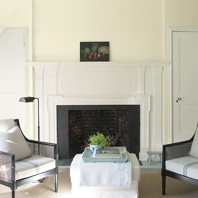 A pretty yellow-green painted wall with a white fireplace flanked by two white doors, with two chairs and a white ottoman in front. A pretty yellow-green painted wall with a white fireplace flanked by two white doors, with two chairs and a white ottoman in front.
