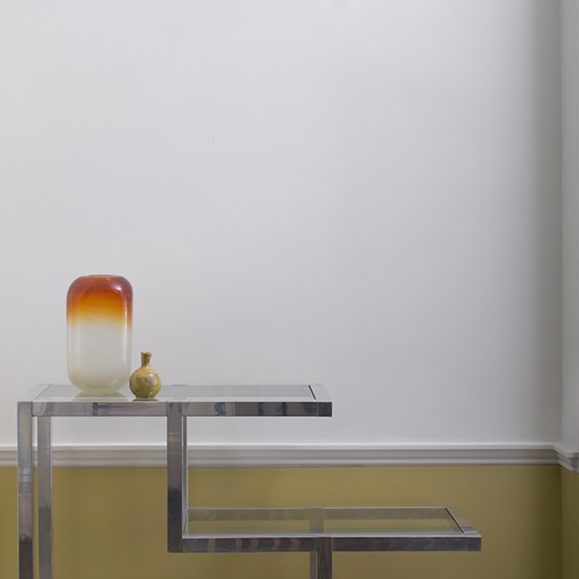 Un mur blanc cassé orné d’une moulure jaune, une table d’appoint moderne et un mobile suspendu au plafond.