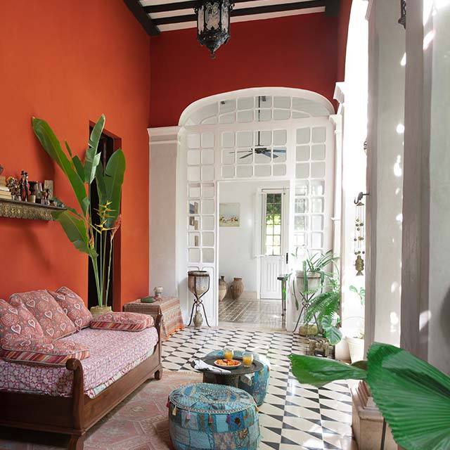 Véranda avec murs orangés; colonnes, moulures et portes blanches; sofa rose pâle; poufs bleus et plancher à motifs noir et blanc.