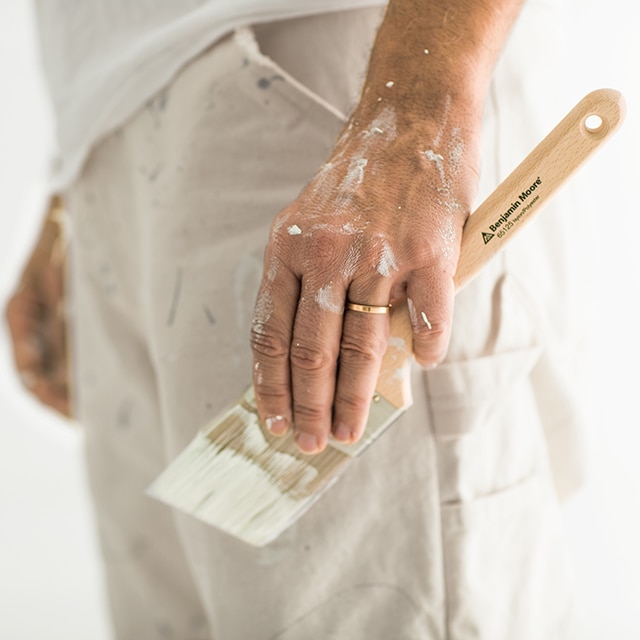 Vue latérale de la moitié inférieure d’un peintre tenant dans sa main gauche tachée de blanc un pinceau. Vue latérale de la moitié inférieure d’un peintre tenant dans sa main gauche tachée de blanc un pinceau.